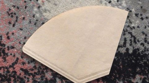 Ein Teppich hat einen Wachsfarbigen Fleck, während ein Papiertuch daneben liegt, um den Fleck zu entfernen.