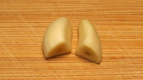 Zwei Knoblauchzehen liegen auf einem Holzbrett und können zur Bekämpfung von Pickeln verwendet werden.