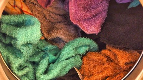 Bunte, weiche Handtücher liegen zusammen in einer Waschmaschine und warten auf das Waschprogramm, um frisch gewaschen zu werden.