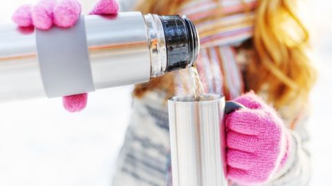 Eine Thermoskanne wird in eine Tasse gegossen, während die Person in warmer Winterkleidung steht.