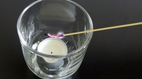 Eine Glasvase mit einer Teekerze wird mit einem Streichholz angezündet, um eine gemütliche Atmosphäre zu schaffen.