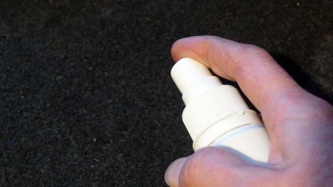 Eine Hand hält eine Sprühflasche, die auf einen schmutzigen Auto-Innenraum zeigt, um die ausgelaufene Milch zu reinigen.
