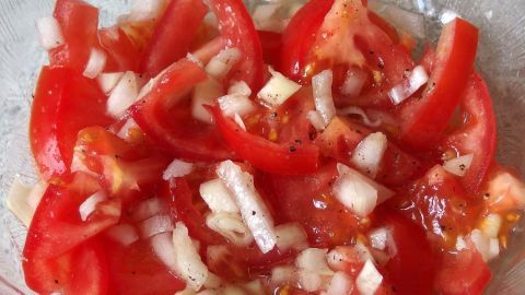 In einer Glasschüssel liegt frischer Tomatensalat mit gehackten Zwiebeln, bereit zum Servieren.