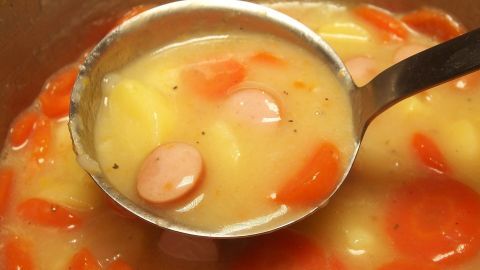 Schnell ist es passiert und es ist zu viel Salz im Essen gelandet. Dieser Tipp hilft, dass das Essen nicht versalzen schmeckt. Ein Löffel nimmt eine milchige Suppe mit Karotten und Würstchen auf, die in einem Topf zubereitet wird. Versalzene Speisen können den Genuss mindern.