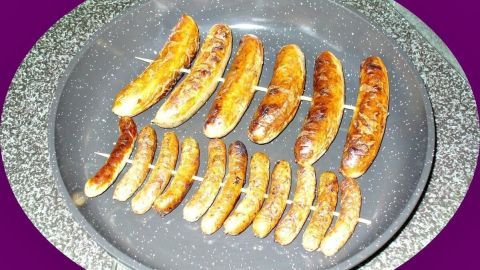 Auf einem Grill liegen Nürnberger Würstchen, die gleichmäßig gebräunt sind, bereit zum Servieren im Freien.