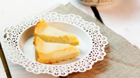 Mit Gelierzucker wird die Masse für Käsekuchen stabiler und fällt nach dem Backen nicht zusammen. Ein splitterförmiger Käsekuchen auf einer filigranen weißen Servierplatte liegt neben einem Zuckergefäß auf einem hellen Tisch.