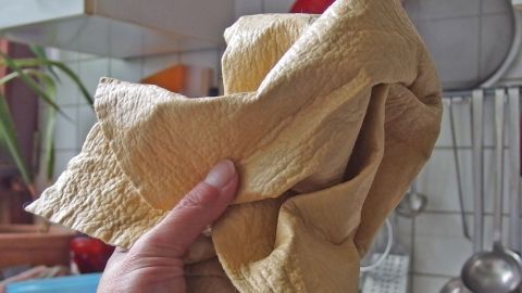 Ein Fensterleder wird fest gehalten, während es in einer Küchenumgebung zum Abwischen von Oberflächen genutzt wird.