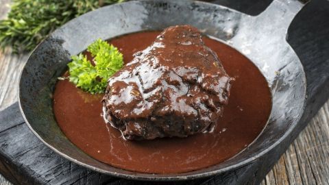 Saftigem Fleisch in dunkler Soße liegt in einer Pfanne, umgeben von frischem Kräuter und rustikalem Hintergrund.