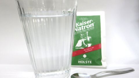 Ein Glas Wasser steht neben einer Tüte Kaiser-Natron und einem Löffel, bereit zur Anwendung gegen Blasenentzündung.
