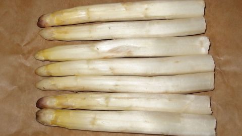Weißer Spargel liegt auf einem Backblech aus Papier und wartet darauf, im Ofen garen zu werden.