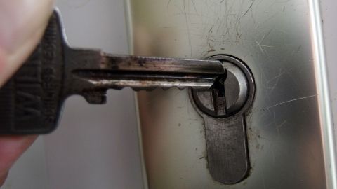 Ein abgebrochener Schlüssel steckt teilweise im Schloss einer metallischen Tür. Eine Hand versucht, ihn herauszuziehen.