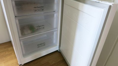 Mit diesem Tipp kann man das Gefrierfach ganz leicht von zu viel gebildetem Eis befreien. Ein Gefrierfach mit Eisbildung wird geöffnet, um das überschüssige Eis zu entfernen. Die Umgebung zeigt einen Holzfußboden.