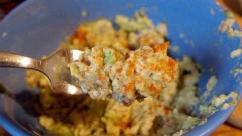 Eine grüne Avocado-Creme liegt in einer blauen Schüssel, während ein Löffel sie portioniert und servierbereit wirkt.