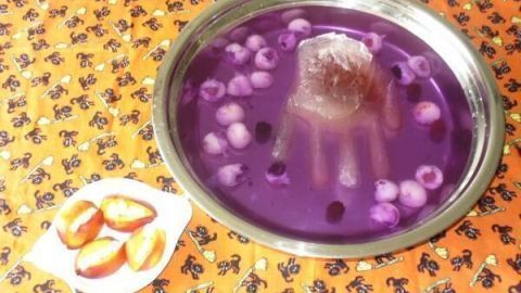 Eine blutige Hand aus Eis schwimmt in einer lila Halloween-Bowle, umgeben von üppigen, schaurigen Dekorationen.