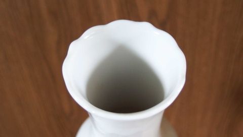 Eine weiße Vase steht auf einem Holzuntergrund, bereit, mit Backpulver gereinigt zu werden, um Vasenränder zu entfernen.