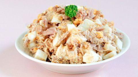 Ein cremiger Thunfischsalat liegt in einer weißen Schüssel, umgeben von einem hellen, rosa Hintergrund.