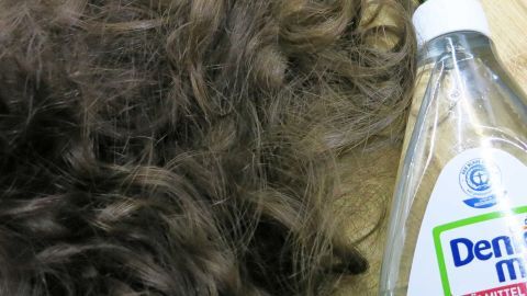 Verfilzte Haare liegen kreuz und quer neben einer Flasche Spülmittel auf einer Holzoberfläche.