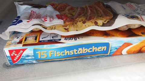 Leichteres Entfernen vom Eis im Gefrierfach: Um das Eis leichter zu entfernen, das Eisfach vor dem Frieren mit Klarsichtfolie auslegen. Ein Gefrierfach enthält eine Verpackung mit 15 Fischstäbchen, umgeben von anderen gefrorenen Lebensmitteln.