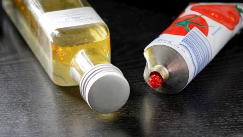 Mit nur ein paar Tropfen Olivenöl bildet sich eine Schutzschicht und das Tomatenmark bleibt länger frisch und haltbar. Eine Tube Tomatenmark steht neben einer Flasche Öl auf einem dunklen Tisch. Tomatenmark wird zur Zubereitung genutzt.