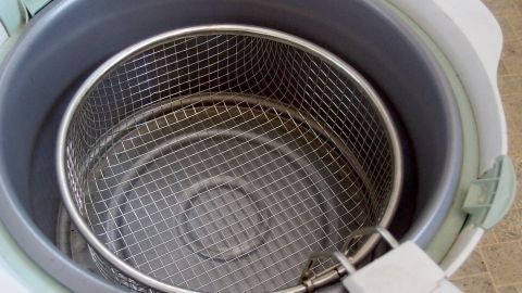 Die mühsame Reinigung deiner Fritteuse kannst du vermeiden, indem du sie einfach für wenige Sekunden einschaltest und danach wieder ausschaltest. Langes, umständliches Kratzen entfällt somit! Eine Friteuse mit einem herausnehmbaren Siebeinsatz steht in einer modernen Küche, bereit zur einfachen Reinigung.