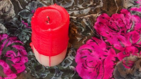 Eine rote Kerze steht auf einem bunten, blumigen Untergrund und hat Wachs verloren, was die Reinigung erforderlich macht.