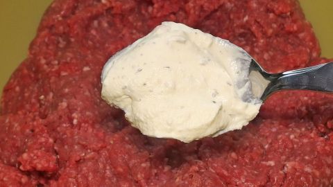 Eine Löffelspitze mit weißem Pulver wird auf rohem Hackfleisch platziert, um Frikadellen ohne Paniermehl und Ei zuzubereiten.