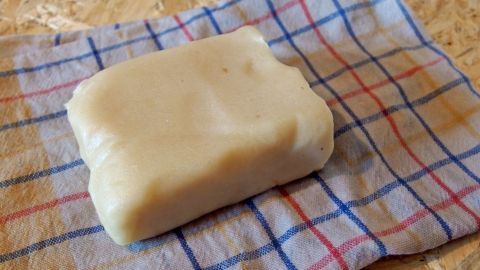 Du hast vom Backen noch Marzipanrohmasse übrig? Dann kannst du das Marzipan in ein feuchtes Küchentuch einschlagen und so eine Weile im Kühlschrank lagern. Ein Stück Marzipan liegt auf einem karierten Küchentuch, bereit zur Lagerung, um seine Frische zu bewahren.