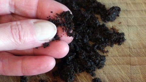 Kaffeesatz wird in der Hand gehalten und bereitet sich für ein Peeling an einem Holzbrett vor.