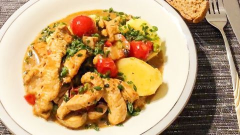 Ein Teller spanischer Geflügelpisto zeigt zarte Hähnchenstreifen mit Tomaten und Kartoffeln in einer würzigen Sauce, begleitet von Brot.