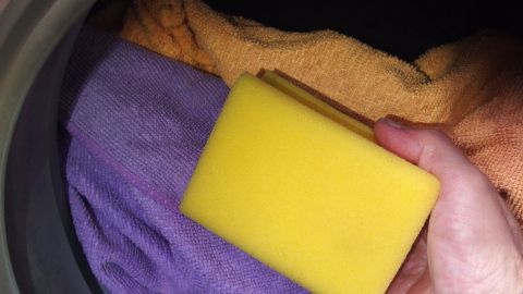 Ein gelber Spülschwamm wird in der Waschmaschine zusammen mit bunten Handtüchern gereinigt.