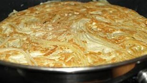Ein goldbraunes Spaghetti-Omelett brät in einer Pfanne, wo die Pasta gleichmäßig verteilt ist und eine knusprige Kruste bildet.