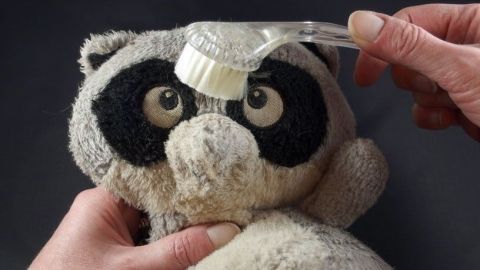 Ein verfilztes Kuscheltier wird mit einer Bürste gepflegt, während Hände zärtlich das Spielzeug festhalten.