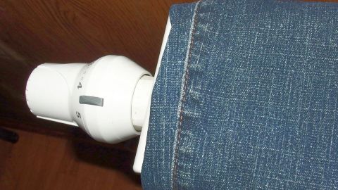 Ein Heizkörper hat eine Jeans über den oberen Teil gelegt, um sie auf der Heizung zu trocknen. Die Umgebung wirkt gemütlich.