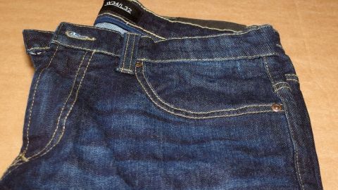 Dunkelblaue Jeans liegen gefaltet auf einer Holzoberfläche und zeigen klare Nähte, die Robustheit und Stil verkörpern.