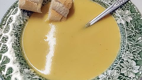 Ein tiefes, grünes Teller zeigt ein cremiges Möhrensüppchen, begleitet von zwei Stückchen Brot und einem Löffel.