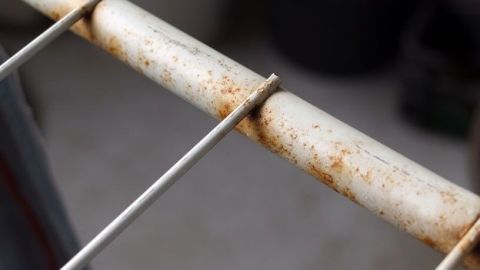 Ein rostiger Metallstab liegt im Fokus, umgeben von unscharfen, dunklen Hintergründen, die eine Werkstatt vermuten lassen.