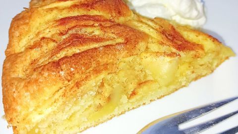 Ein Stück Apfelkuchen liegt auf einem weißen Teller neben einem Klecks Sahne, bereit zum Genießen.
