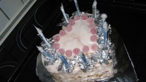 Eine herzförmige Torte mit rosa Zuckerguss und roten Pralinen, umgeben von silberner Folie und blauen Kerzen im Ofen.