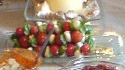 Tomaten-Mozzarella-Spieße sind auf einem Tisch angeordnet, umgeben von Dips und einer Kerze im Hintergrund.