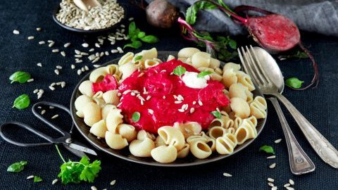 Ein Teller Vollkornnudeln ist mit einer leuchtend roten Rote Beete-Sauce und Kürbiskernen garniert.
