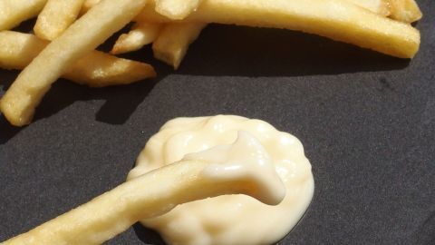 Pommes frites liegen neben einer dünnflüssigen Mayonnaise, die auf einer dunklen Oberfläche serviert wird.