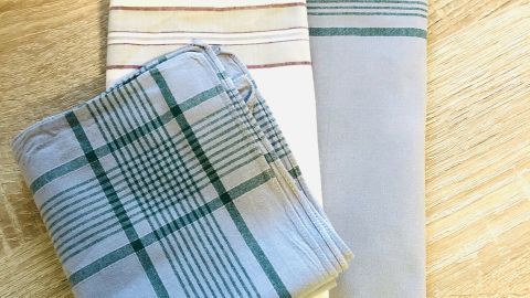 Herrentaschentücher eignen sich sehr gut als preiswerter Ersatz für Stilleinlagen. Wenn man sie bügelt, sind sie sogar desinfiziert und ökologisch ist es auch noch. Drei Herrentaschentücher mit verschiedenen Mustern liegen auf einem Holzuntergrund, bereit zur Verwendung als Stilleinlagen.
