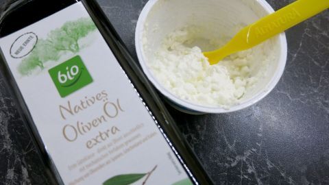 Hier ist eine schöne Idee für einen gesunden und gleichzeitig sättigenden Dip mit wenig Kalorien aus Hüttenkäse und ein wenig feinem Olivenöl. Hüttenkäse wird mit einem gelben Löffel in einer Schüssel angerührt, während eine Flasche Olivenöl daneben steht.
