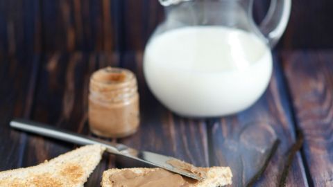 Ein Krug Milch steht neben zwei gerösteten Brotscheiben, die mit Milchmarmelade bestrichen sind, auf einem Holztisch.