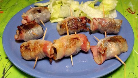 Saftige Pflaumen sind in knusprigem Speck eingewickelt und schön angerichtet auf einem blauen Teller, umgeben von Salat.