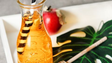 Ein Glas mit einem Diät-Drink aus Apfelessig steht auf einem Tablett, umgeben von einem Blatt und einem Apfel.