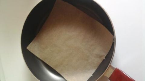 Eine Pfanne liegt auf einer glatten Oberfläche, bedeckt von einem Blatt Backpapier, das fettfreies Braten ermöglicht.