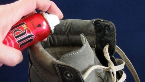 Verhindern von dunklen Flecken in neuen Schuhen mit Haarspray. Ein Hand greift eine Spraydose, die Haarspray auf einen Schuh sprüht, um keine dunklen Flecken zu hinterlassen.