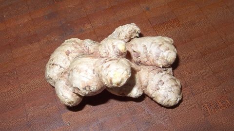 Ein frischer Ingwer mit unregelmäßiger Form liegt auf einer Holzoberfläche, umgeben von natürlicher Küchenausstattung.