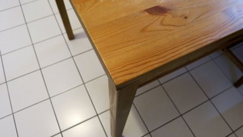 Ein Holztisch mit glatter Oberfläche steht auf einem gefliesten Boden in einem hellen Raum, bereit für eine Auffrischung.